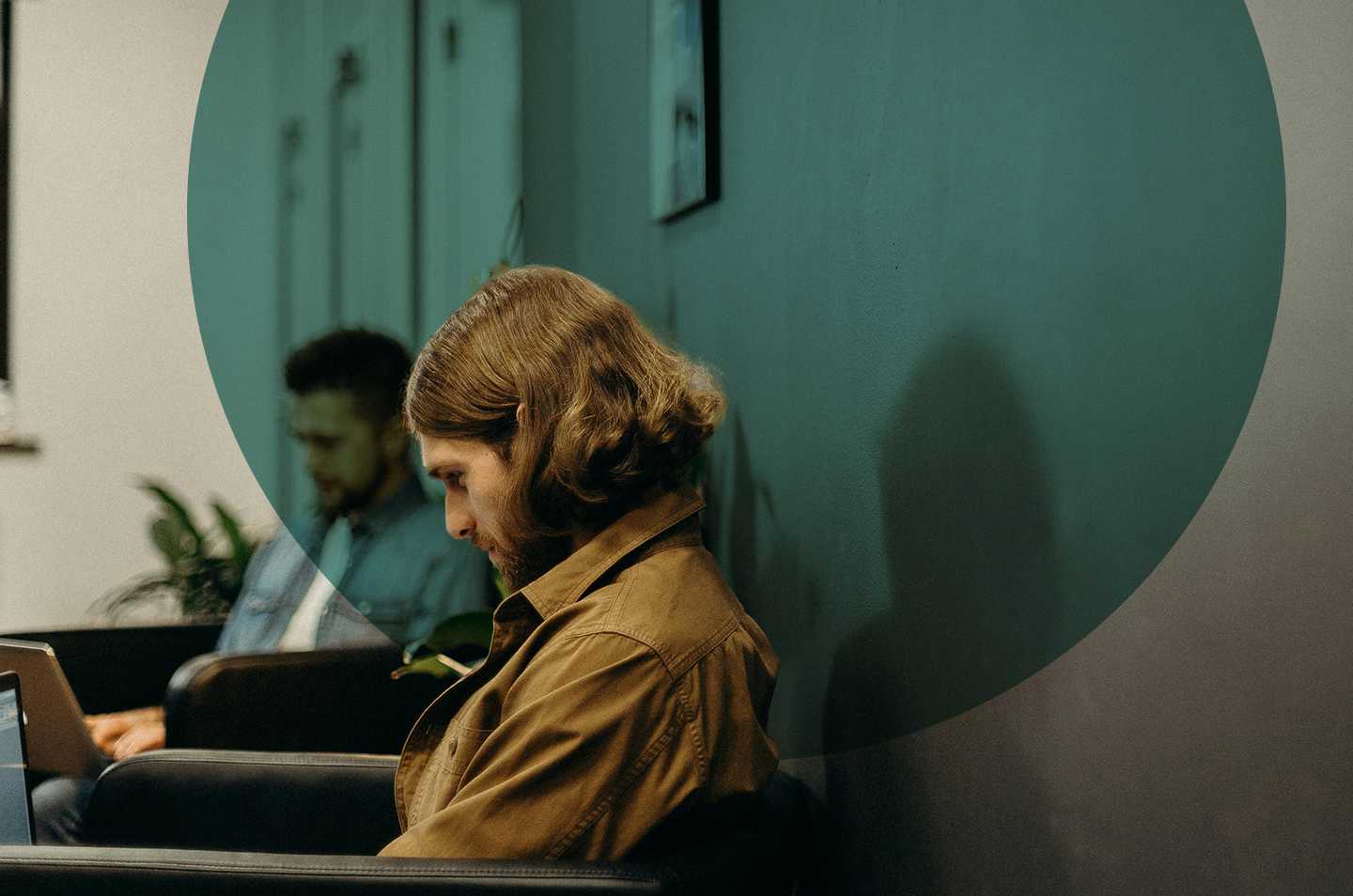 A man sitting against a wall looking down at a laptop