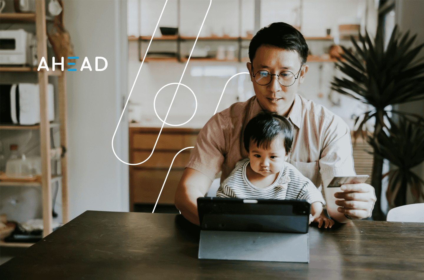a man sitting at a table looking at a tablet with a baby in his lap