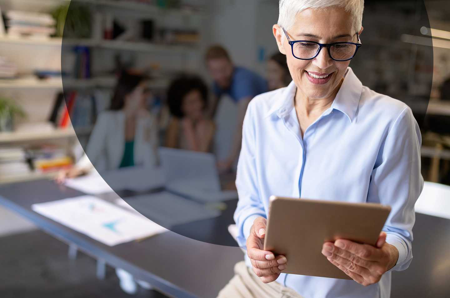 a woman in the foreground looking at a tablet with a group of people in the background